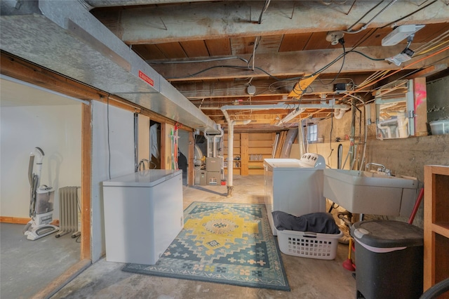 unfinished basement featuring a sink, refrigerator, radiator heating unit, and separate washer and dryer