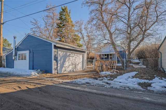 snow covered garage with a detached garage, a gate, and fence