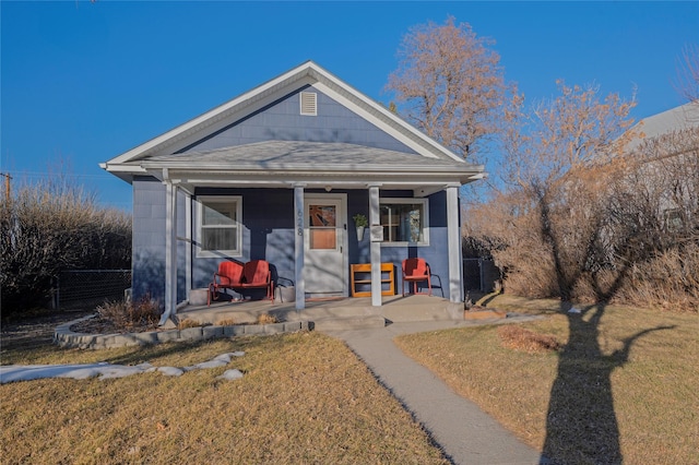 bungalow-style home with covered porch, fence, a front lawn, and roof with shingles