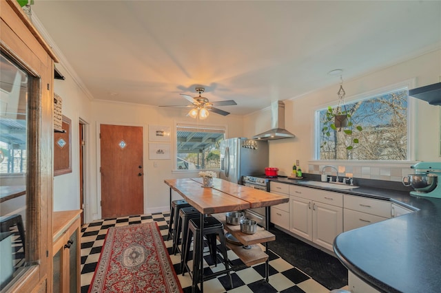 kitchen featuring stainless steel appliances, a sink, crown molding, wall chimney exhaust hood, and dark floors