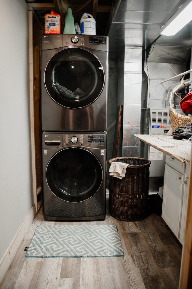 laundry area featuring wood finished floors, stacked washer / drying machine, and baseboards