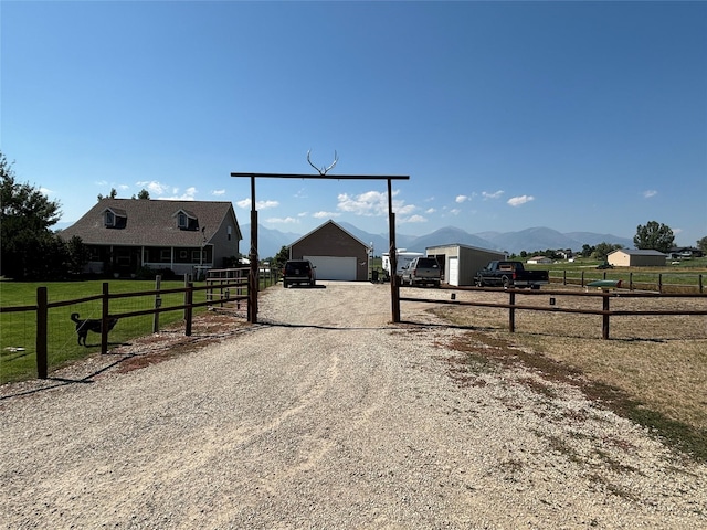 exterior space with a rural view, gravel driveway, fence, an outdoor structure, and a mountain view