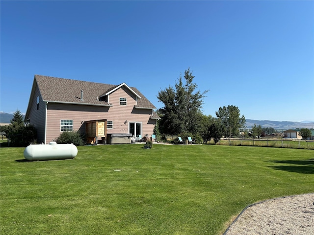 rear view of property featuring fence, a lawn, a mountain view, and roof with shingles