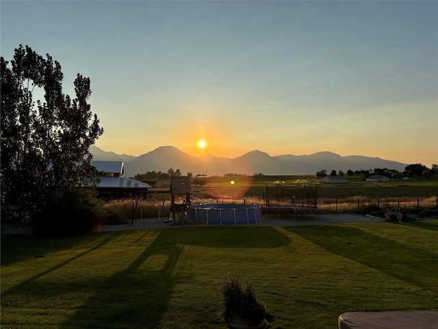 yard at dusk with a mountain view, a trampoline, and fence