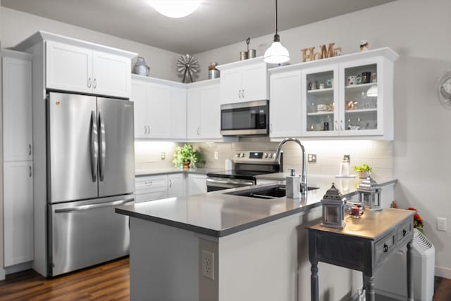 kitchen featuring a peninsula, a sink, glass insert cabinets, appliances with stainless steel finishes, and white cabinetry