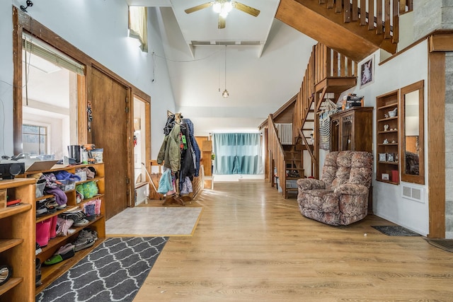 foyer featuring visible vents, stairs, a towering ceiling, wood finished floors, and a ceiling fan