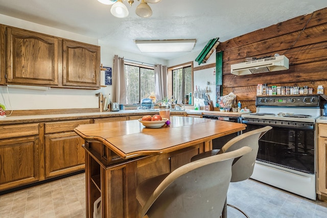 kitchen with under cabinet range hood, range with electric cooktop, brown cabinetry, and light floors