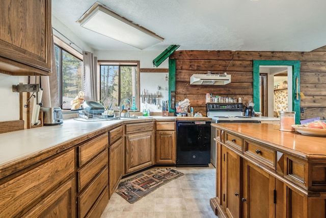 kitchen featuring under cabinet range hood, a sink, black dishwasher, wood walls, and light countertops