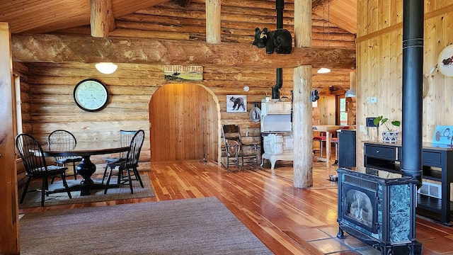 dining space with arched walkways, high vaulted ceiling, wood finished floors, and a wood stove