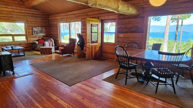 dining area with hardwood / wood-style floors, lofted ceiling with beams, a wealth of natural light, and log walls