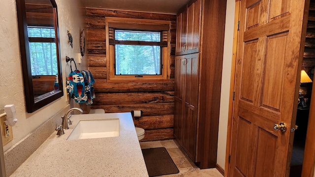 bathroom with stone tile flooring, toilet, a textured wall, and a sink