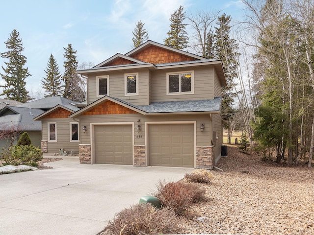 craftsman-style home with a shingled roof, concrete driveway, a garage, stone siding, and central air condition unit