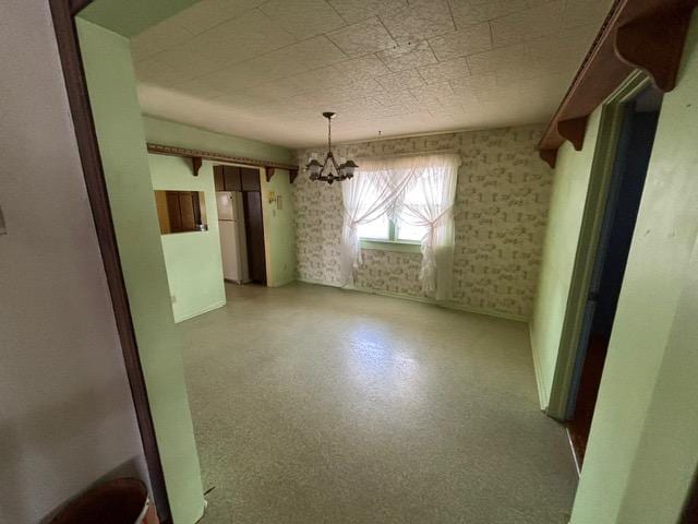 unfurnished dining area with baseboards, a chandelier, and wallpapered walls