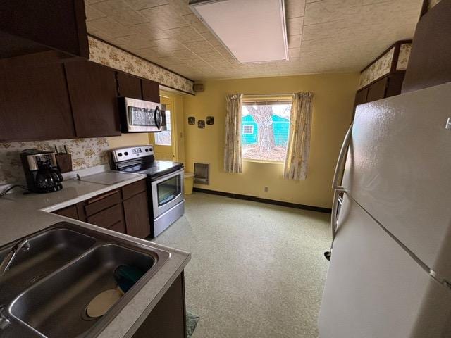 kitchen featuring baseboards, a sink, light countertops, dark brown cabinets, and appliances with stainless steel finishes