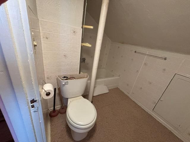 bathroom with tile walls, toilet, and a bath