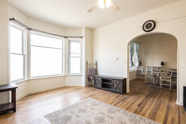 sitting room featuring a ceiling fan, wood finished floors, arched walkways, and baseboards