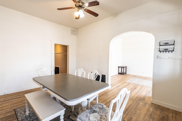 dining area with visible vents, baseboards, wood finished floors, arched walkways, and a ceiling fan