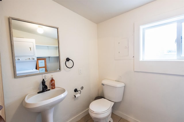 half bathroom featuring baseboards, a sink, tile patterned flooring, stacked washer and dryer, and toilet