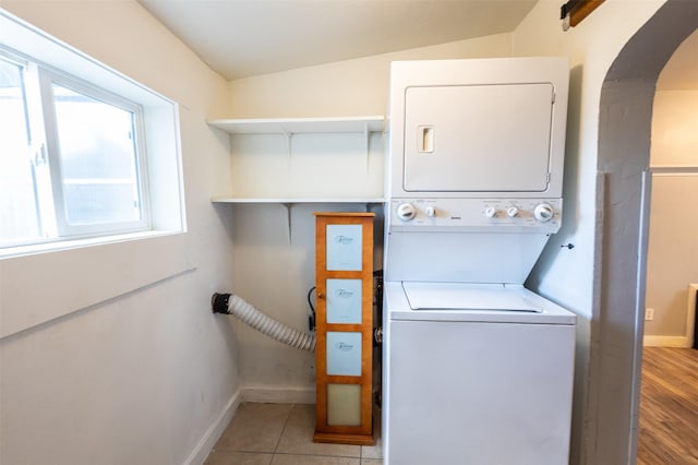 washroom featuring baseboards, laundry area, arched walkways, tile patterned flooring, and stacked washer / drying machine