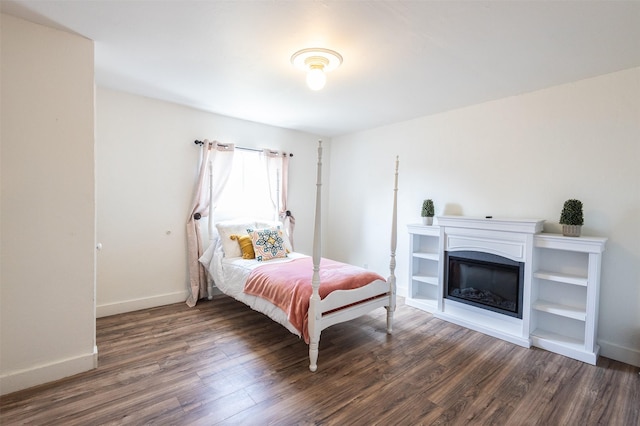 bedroom with a glass covered fireplace, wood finished floors, and baseboards