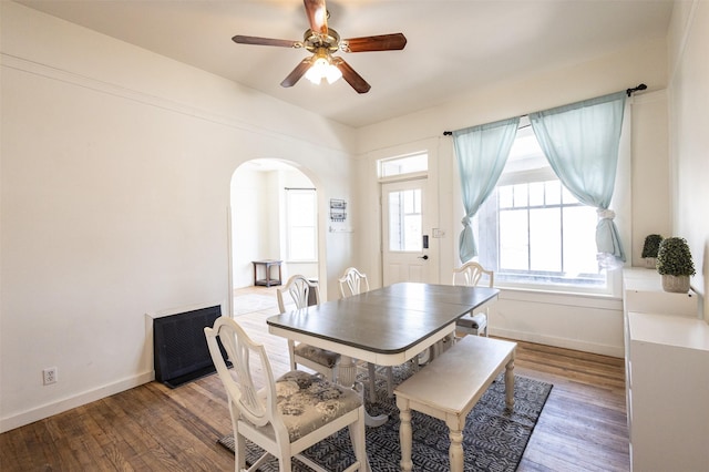 dining space with arched walkways, a ceiling fan, baseboards, and wood finished floors