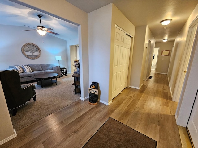 hallway featuring baseboards, lofted ceiling, and light wood-style floors