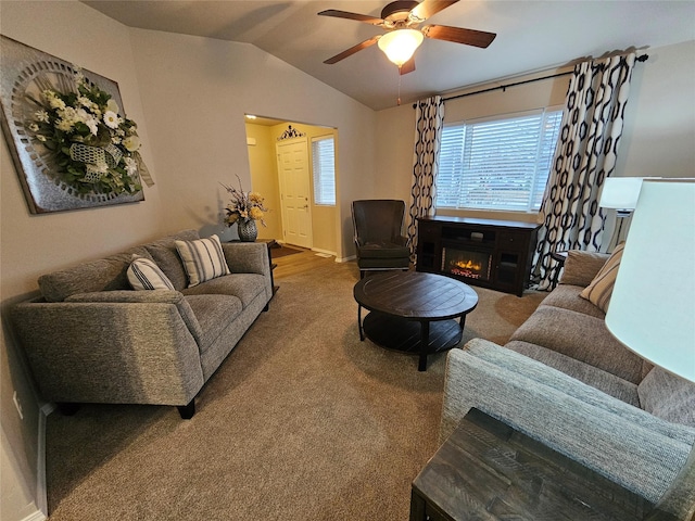 living area with a glass covered fireplace, vaulted ceiling, carpet flooring, and a ceiling fan