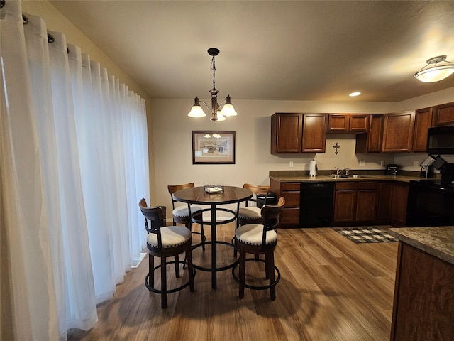 kitchen with dark countertops, dark wood-type flooring, a chandelier, black appliances, and a sink