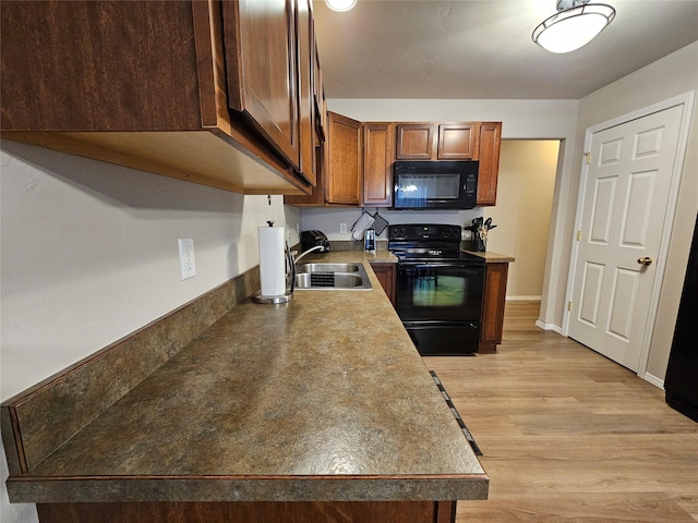 kitchen featuring black appliances, a sink, brown cabinetry, light wood finished floors, and baseboards