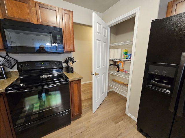 kitchen featuring brown cabinets, light wood finished floors, black appliances, light countertops, and baseboards