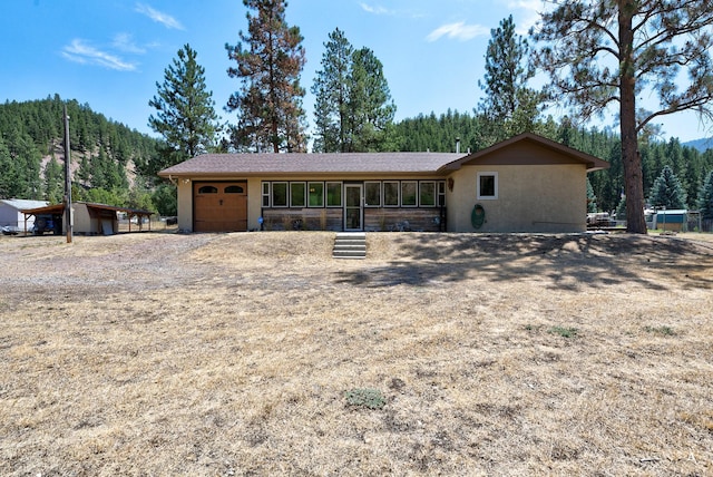 view of front of home featuring stucco siding, driveway, a view of trees, and an attached garage