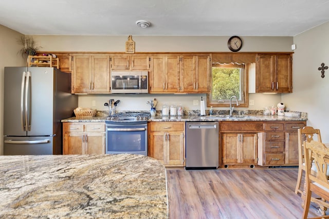 7415 Wildcat St, Helena, MT 59602 - kitchen with stainless steel appliances, a sink, light wood-type flooring, light stone countertops, and brown cabinetry