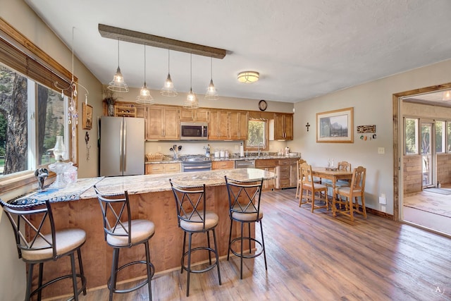 7415 Wildcat St, Helena, MT 59602 - kitchen featuring appliances with stainless steel finishes, wood finished floors, a peninsula, brown cabinets, and a kitchen breakfast bar