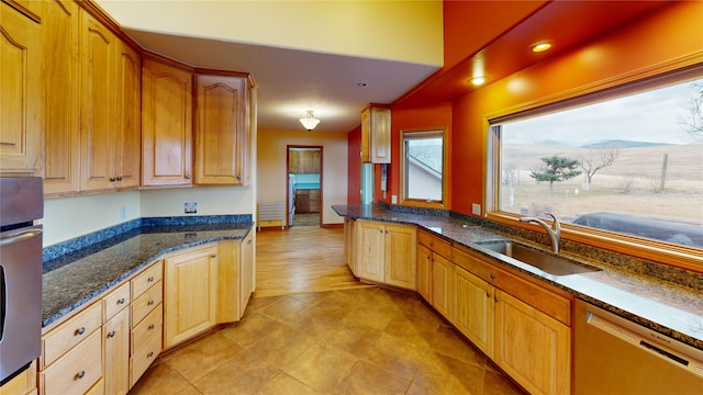 kitchen featuring a sink, dark stone countertops, light tile patterned flooring, and stainless steel appliances