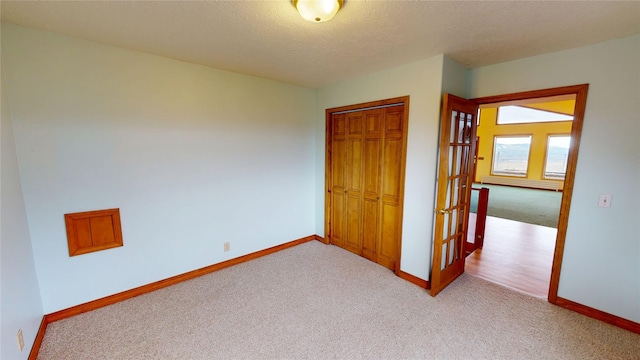 unfurnished bedroom featuring a textured ceiling, light colored carpet, a closet, and baseboards