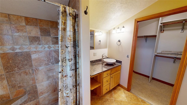 bathroom with a walk in closet, vaulted ceiling, a tile shower, a textured ceiling, and vanity