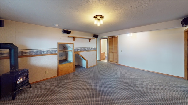 carpeted empty room with wallpapered walls, a textured ceiling, a wood stove, and baseboards