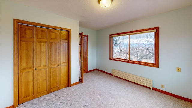 unfurnished bedroom with light carpet, a closet, a baseboard heating unit, and baseboards