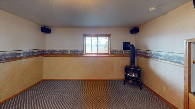 unfurnished room featuring wallpapered walls, a wood stove, carpet flooring, and a wainscoted wall