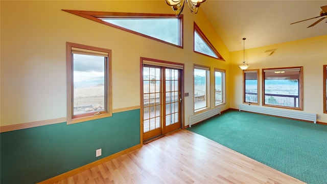 empty room featuring a baseboard heating unit, ceiling fan with notable chandelier, wood finished floors, and high vaulted ceiling