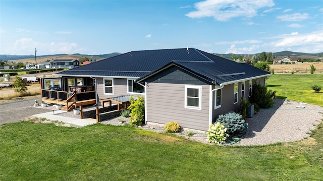 back of property with central AC unit, a lawn, a deck with mountain view, and metal roof