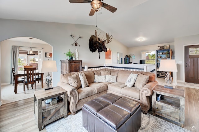 living room featuring baseboards, vaulted ceiling, light wood-style floors, arched walkways, and a ceiling fan