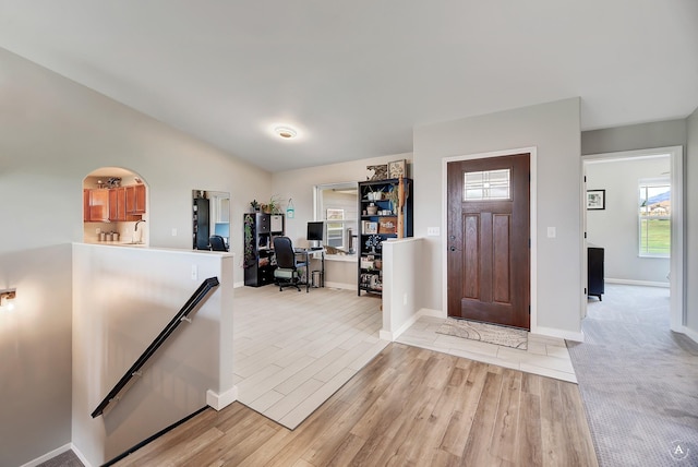 foyer featuring baseboards, arched walkways, lofted ceiling, and light wood-style flooring