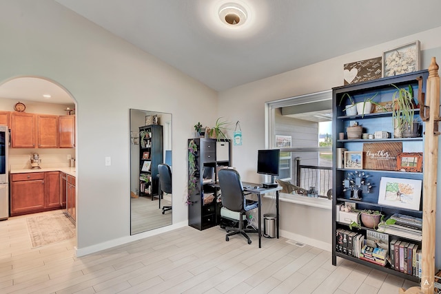 office area featuring vaulted ceiling, baseboards, arched walkways, and light wood finished floors