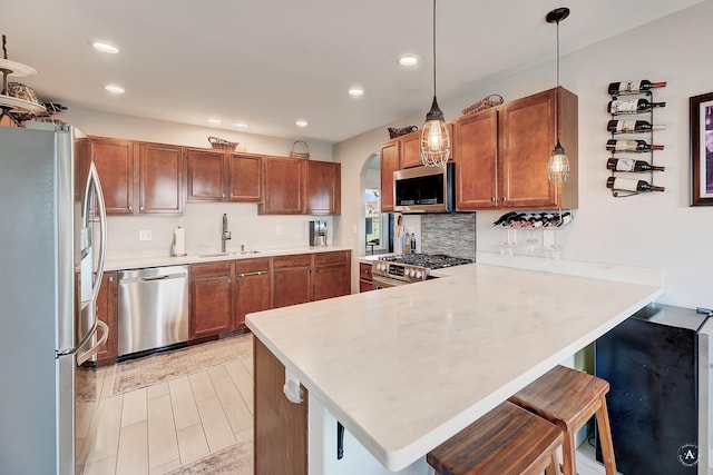 kitchen featuring brown cabinets, appliances with stainless steel finishes, a peninsula, arched walkways, and a sink