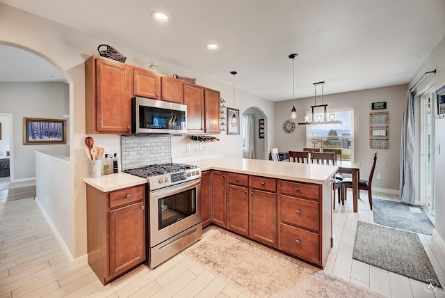 kitchen with backsplash, stainless steel appliances, arched walkways, a peninsula, and light countertops