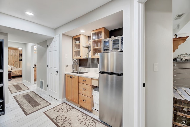 kitchen with visible vents, glass insert cabinets, light countertops, freestanding refrigerator, and a sink