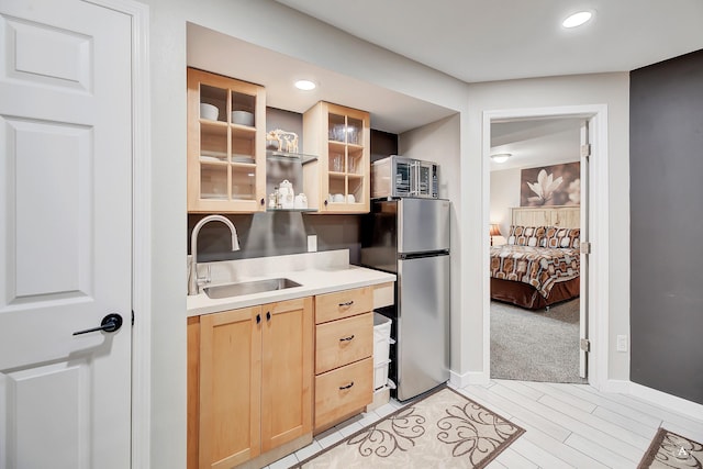 kitchen with light brown cabinets, glass insert cabinets, light countertops, freestanding refrigerator, and a sink