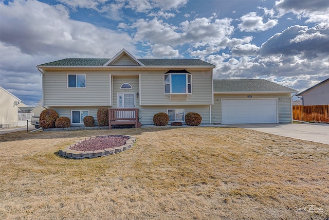 split foyer home featuring a front lawn, driveway, an attached garage, fence, and roof with shingles