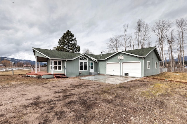 view of front facade with a shingled roof, an attached garage, concrete driveway, and fence